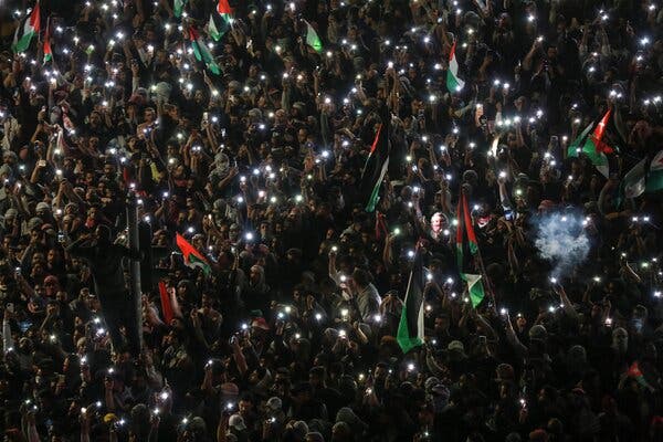 A dense crowd waves Palestinian flags and hold up cellphone lights.