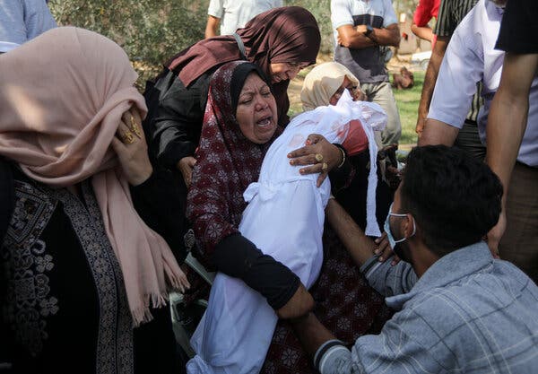 A distressed-looking woman cradles a small body shrouded in white as others cry around her.
